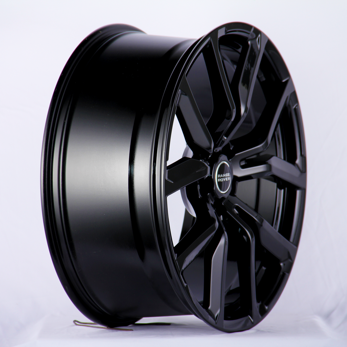 A black alloy wheel with a sleek, glossy finish and multi-spoke design sits upright in a well-lit studio. Text on the center cap reads: "RANGE ROVER."
