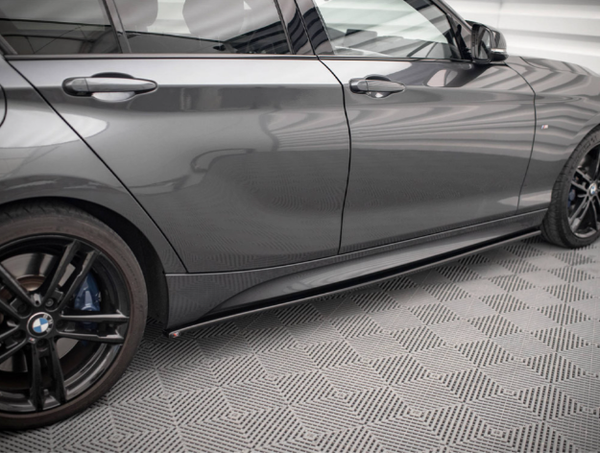 A grey car with sleek side panels is stationary on a patterned, textured floor. The vehicle features black wheels and distinct handles, reflecting a bright indoor environment.