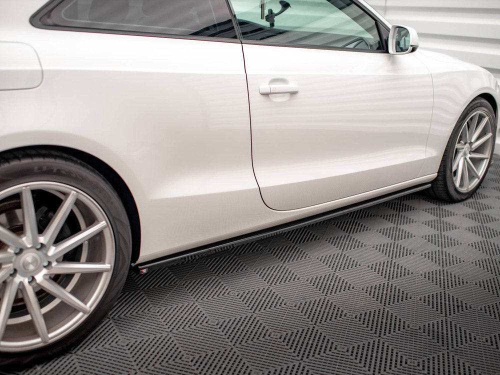 A white car parked on a patterned garage floor, viewed from the side, revealing its sleek design, shiny wheels, and closed door. The setting has a modern and clean appearance.
