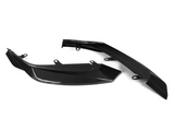 Two black carbon fiber car parts, resting on a white background. Each piece features mounting brackets, showcasing an intricate weave pattern typical of carbon fiber components.