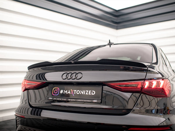 A black Audi car is parked indoors, facing away. The taillights are illuminated, and the license plate reads "#MAXTONIZED Porsche Wien Hietzing." The setting has white panel walls.