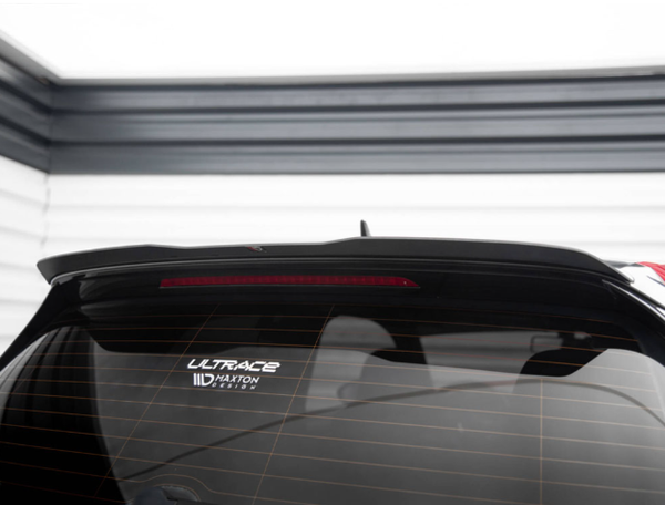 A car rear window with a high-mounted brake light displays two stickers reading "ULTRACE" and "Maxton Design." It's parked against a wall with horizontal black and white stripes.