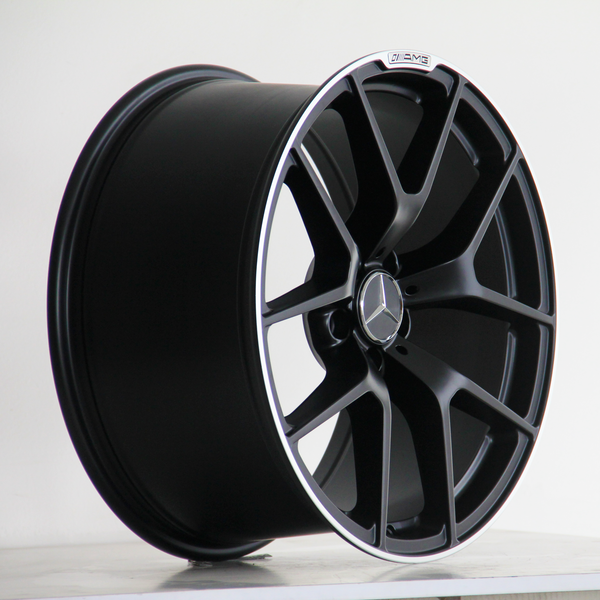 A black alloy wheel with multiple spokes features a Mercedes emblem in the center. It rests on a plain surface. The text "AMG" is visible on the wheel's rim.