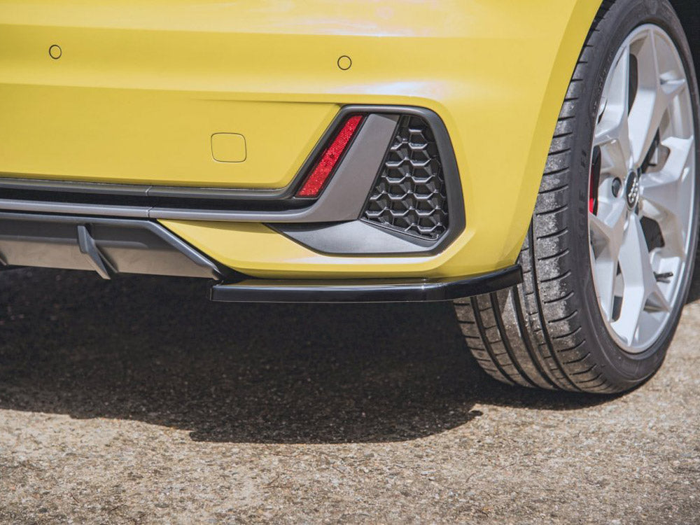 A yellow car's rear bumper features a red reflector, black trim, and hexagonal grille pattern. The context shows a parked car on a sunlit asphalt surface.