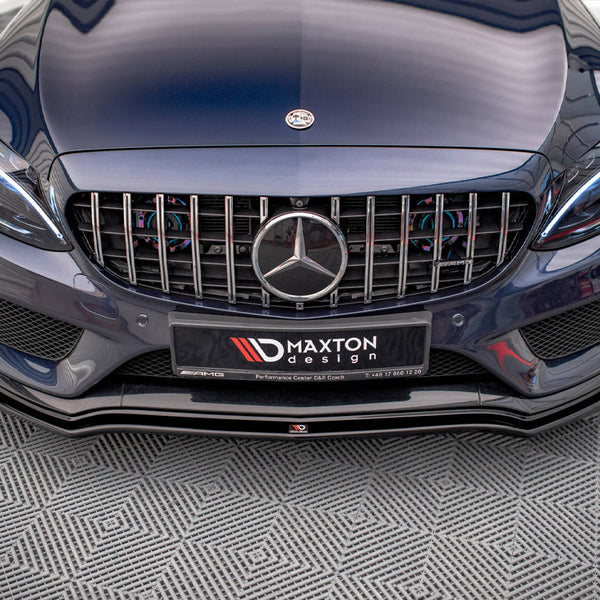 A dark blue car with a prominent front grille displaying a circular emblem sits on a textured floor. The license plate reads "MAXTON design" with contact information and AMG branding.