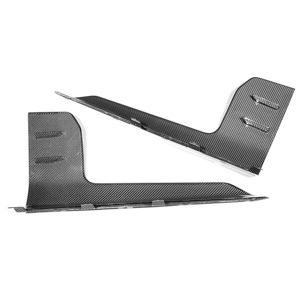 Two carbon fiber automotive parts lie on a plain white background, showcasing a sleek, angular design with smooth finishes and textured surfaces, likely intended for aerodynamic purposes.