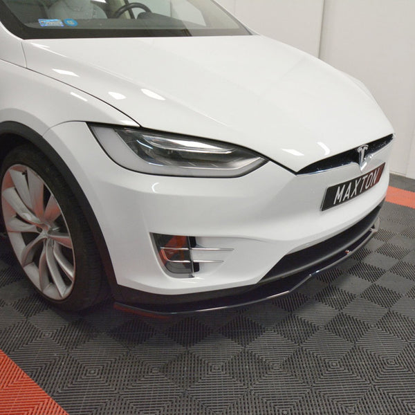 A white Tesla car is stationary, showcasing a front view on a black-and-red checkered floor. The license plate reads "MAXTON."