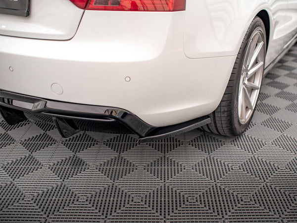 A white car's rear bumper and wheel are shown on a textured, gray, diamond-patterned floor. The car features a black diffuser underneath the bumper, adding sporty detailing.