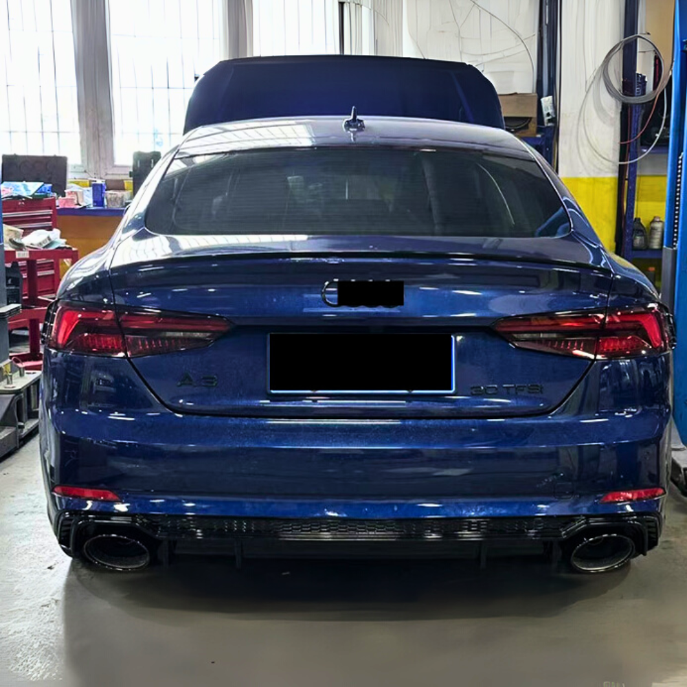 A blue car is parked in an automotive workshop with its hood open. Shelves, tools, and equipment are visible around it. Text on the car reads "A6" and "50 TFSI."