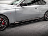 A sleek, silver car is parked on a textured gray floor. It features red brake calipers, sporty black wheels, and a side emblem with colored stripes.
