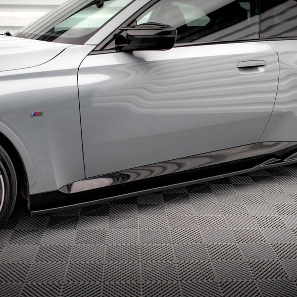 A sleek, silver car is parked on a textured gray floor. It features red brake calipers, sporty black wheels, and a side emblem with colored stripes.