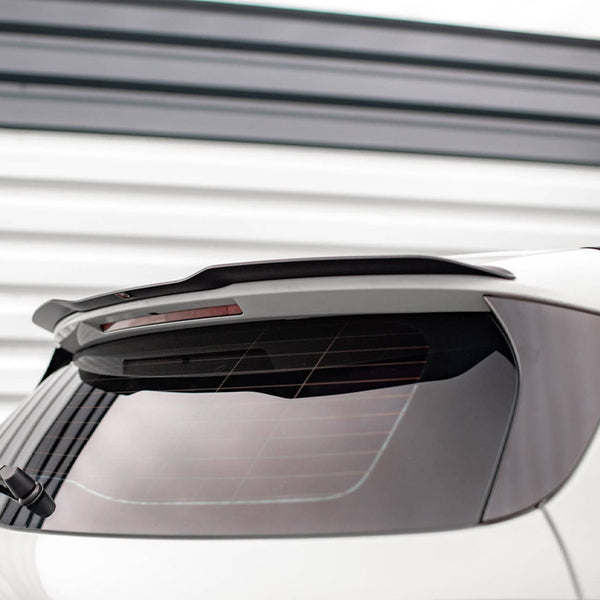 Car rear window with a partially visible wiper and a spoiler above. The vehicle is parked in front of a white, horizontal-striped wall, providing a modern backdrop.