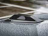 A carbon-fiber shark fin antenna rests on a car roof, covered with water droplets, in a parking lot with painted lines visible in the background.