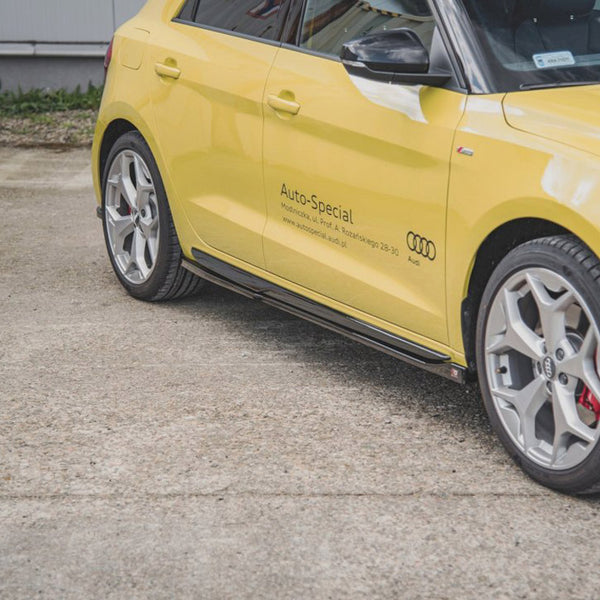 A yellow Audi car is parked on a concrete surface. The side displays: "Auto-Special" with contact details and the Audi logo. A building and grass are visible in the background.
