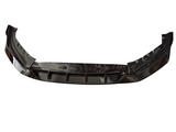 A black car bumper or front splitter, slightly curved with angular design features, is isolated against a white background. It appears shiny and reflective, with no additional elements visible.