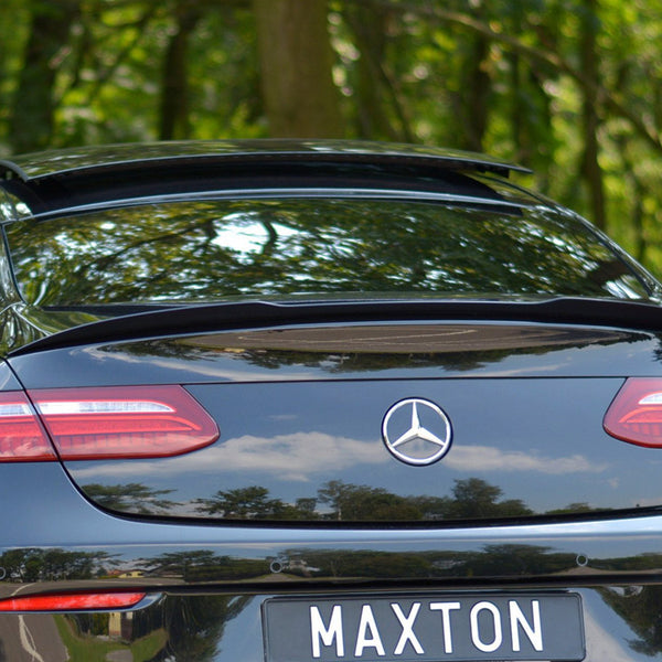 The black car is parked with a slightly open sunroof, displaying a Mercedes emblem and a license plate reading "MAXTON," surrounded by a lush forest environment.