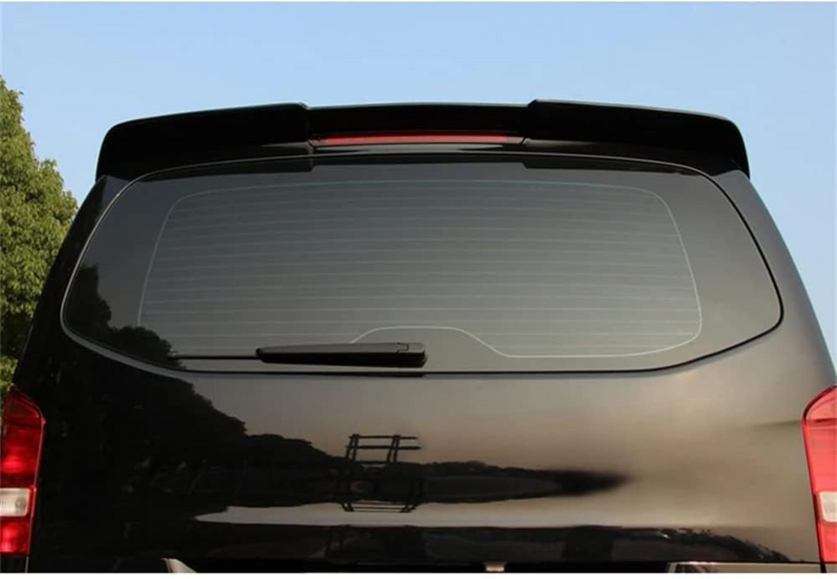 A black car with a rear window features a wiper and a spoiler on top. It is parked outdoors against a backdrop of trees and a clear blue sky.