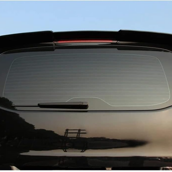 A black car with a rear window features a wiper and a spoiler on top. It is parked outdoors against a backdrop of trees and a clear blue sky.