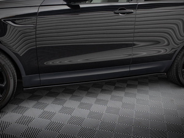 A black SUV side view shows reflections on its surface with "DISCOVERY" text near the front door. It stands parked on a textured gray floor, showcasing two tires.