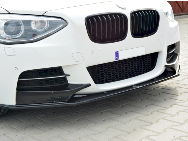 The front of a white car with a sleek black grille and bumper, parked on a paved surface. A license plate displays "PL."