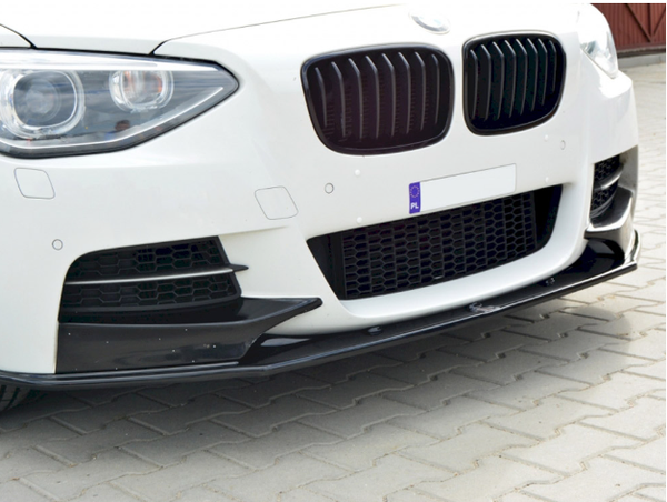 The front of a white car with a sleek black grille and bumper, parked on a paved surface. A license plate displays "PL."