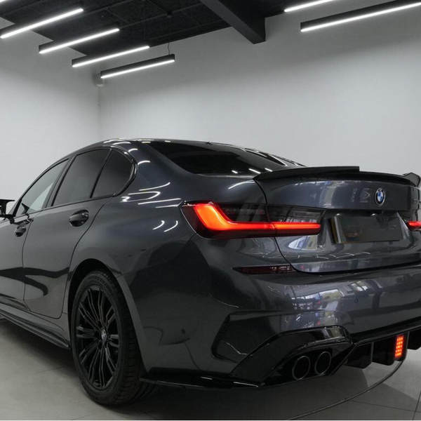A dark gray car with tinted windows is parked in a well-lit room, showcasing sleek tail lights and a prominent rear bumper design.