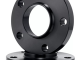 Two black metal flanges with multiple bolt holes are stacked vertically; the top flange is positioned upright. The setting appears to be a plain white studio background.