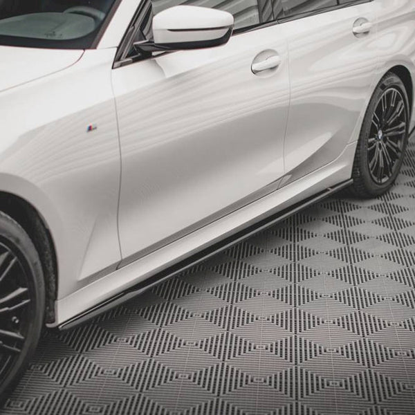 A white car with black alloy wheels is parked on a textured, patterned floor within a room with white walls.