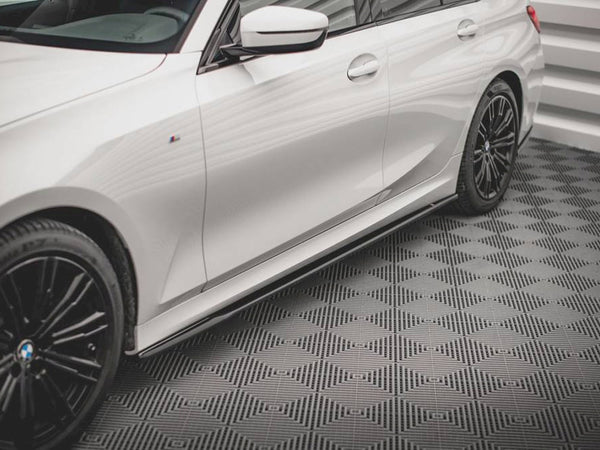 A white car with black alloy wheels is parked on a textured, patterned floor within a room with white walls.