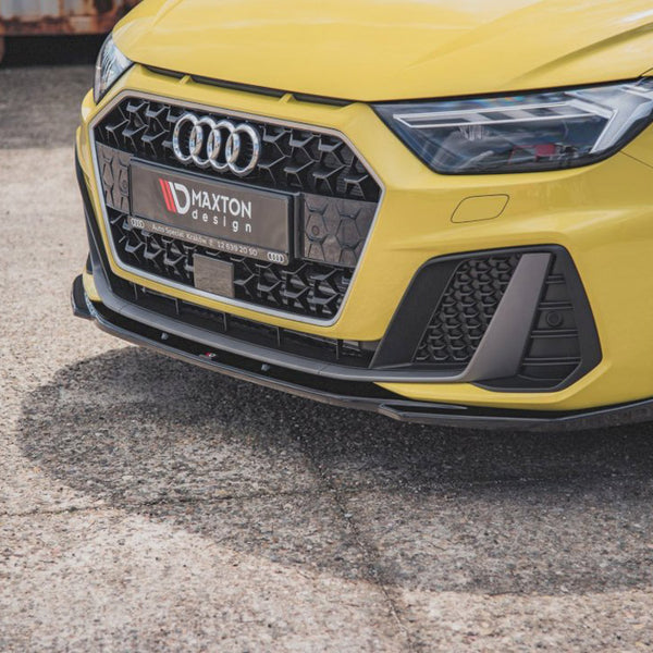 A yellow car's front view, featuring an Audi logo, sporty grille, and headlight on a textured pavement. The license plate reads "MAXTON design AUTO SPECIAL KRZYSZ 72 859 20 50."