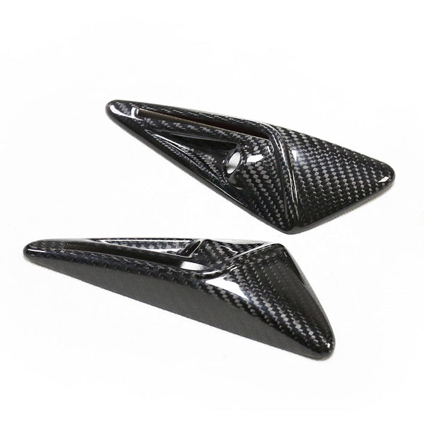 Two sleek, black carbon fiber triangular objects rest on a white surface, featuring glossy finishes with smooth, sharp edges and recessed grooves.