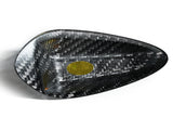 Triangular carbon fiber bowl with a glossy weave texture rests on a white surface. A small, gold oval sticker with text is inside, adding contrast to the dark material.