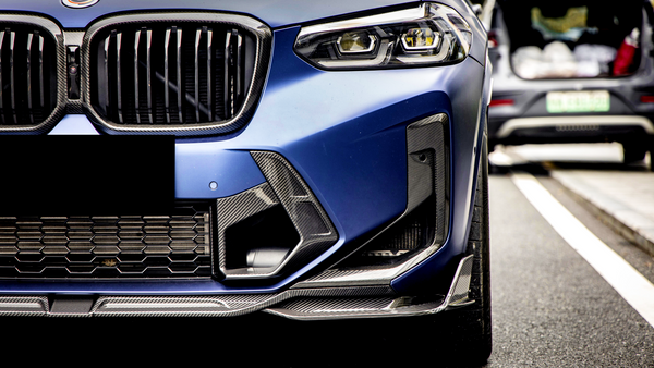 A blue car's front bumper and grille, with a sleek design, is parked on a street lined with cars. The focus is on its headlight and intricate grille pattern.