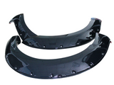 Two glossy black car fender flares lay on a plain white background. Each flare features multiple rivet holes along the curved edges, designed for vehicle installation.