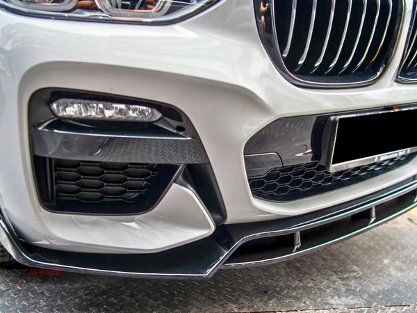 A car's front bumper with a grille and headlights sits on textured pavement. The bumper features honeycomb vents and sleek black accents, illustrating a sporty design.