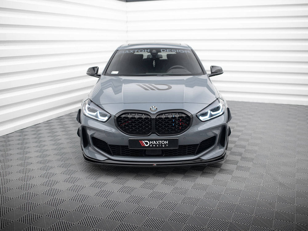 A gray BMW sports car with illuminated headlights is parked in a modern, white-walled showroom. The windshield displays "MAXTON DESIGN." Checkered pattern on the floor.
