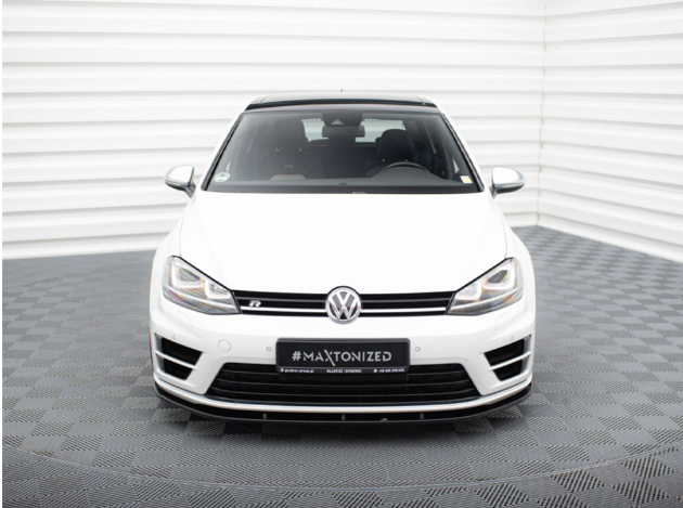 A white Volkswagen car is parked in a well-lit showroom with geometric patterned flooring and white walls. The license plate reads "#MAXTONIZED" with additional details below.
