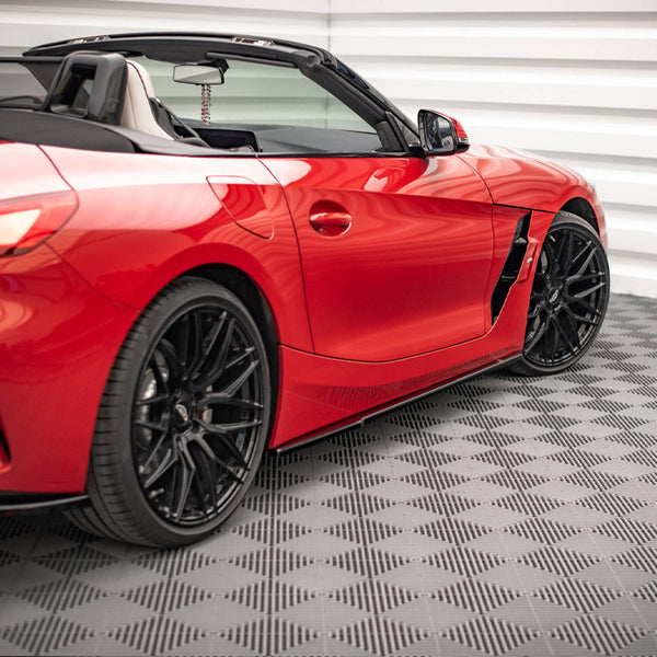 Red convertible sports car, parked, showcasing black wheels and sleek design. It sits on a patterned floor in a white-paneled garage.