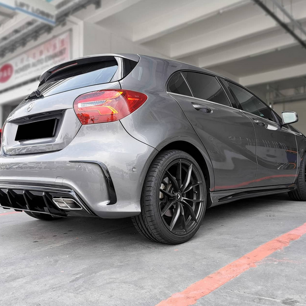 A silver hatchback is parked in a garage-like setting, emphasizing its rear design and black alloy wheels. Surrounding industrial structures create a modern, urban backdrop. No text is visible.