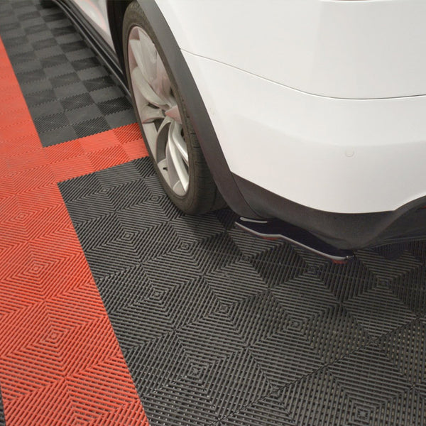 A white car's rear is parked on a checkered black and red garage floor. The car's tire is visible, and there are no visible markings or objects around.