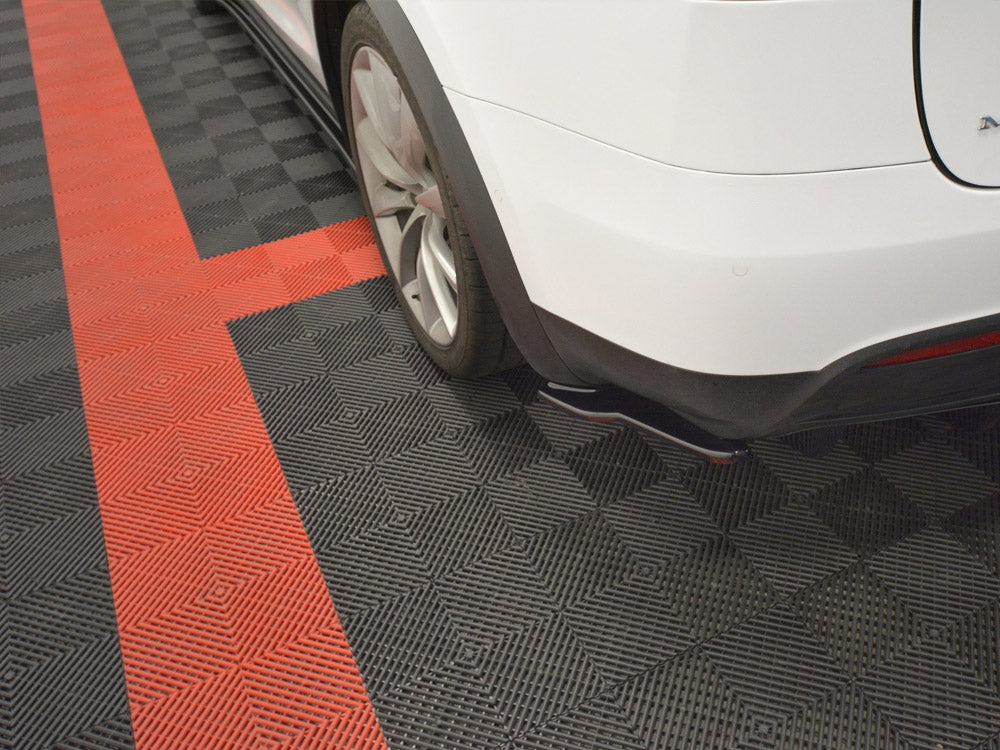 A white car's rear is parked on a checkered black and red garage floor. The car's tire is visible, and there are no visible markings or objects around.