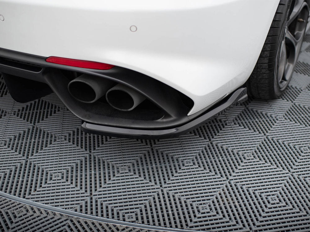 Car exhaust pipes protrude from the rear of a white vehicle, parked on a gray, textured, diamond-patterned surface, with a visible rear tire and partial red reflector.