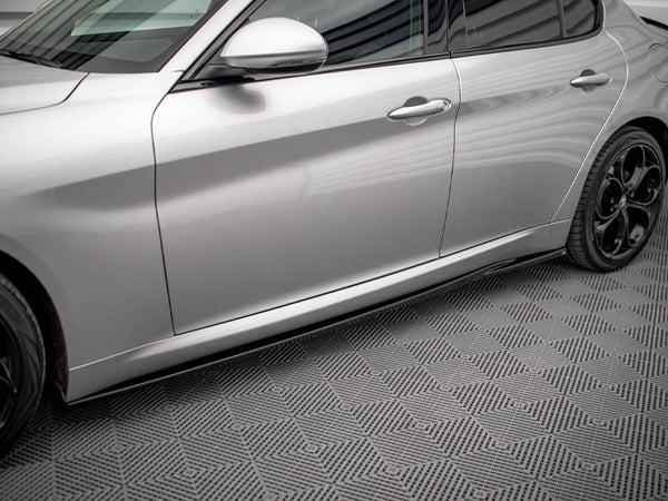 A silver car with sleek, aerodynamic design is parked on a textured, geometric-patterned floor. The car's side doors and black alloy wheels are visible, reflecting soft lighting.