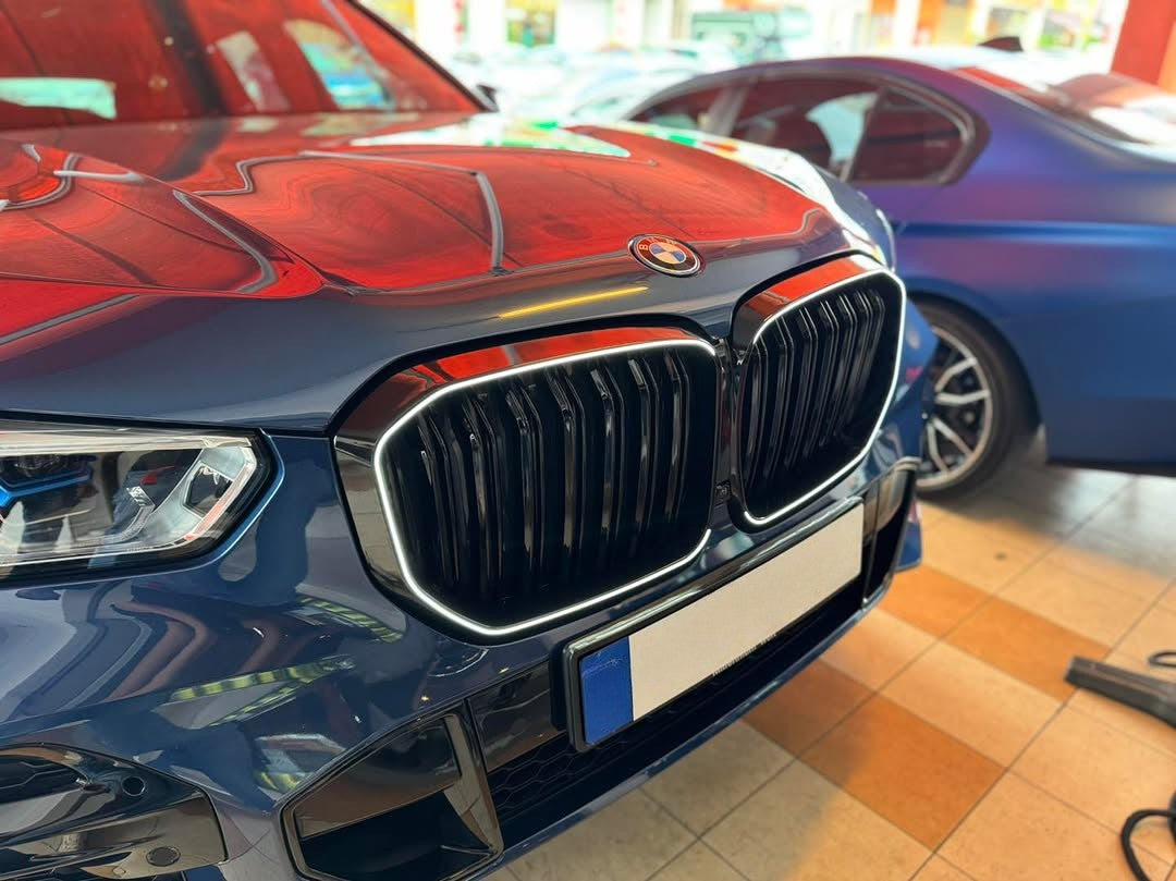 A shiny blue car features a prominent front grille and logo, parked next to another blue car in an indoor showroom with a tiled floor and overhead lighting.