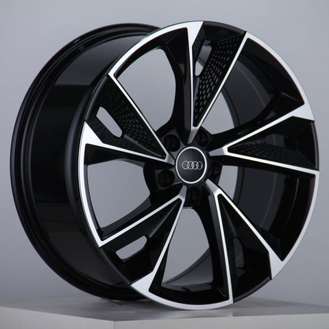 A glossy, black alloy wheel features silver accents and the Audi logo at the center, displayed on a neutral gray background with a studio setting.
