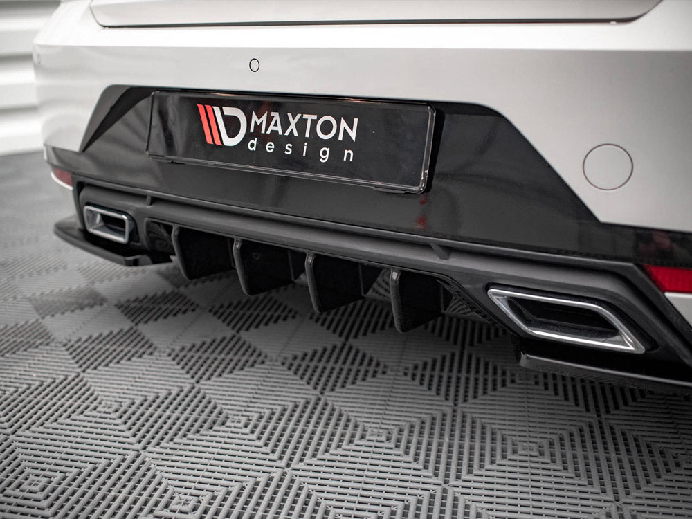 Car's rear bumper features dual exhaust outlets and diffuser; black "MAXTON design" license plate is displayed; parked on textured gray flooring in an indoor setting.