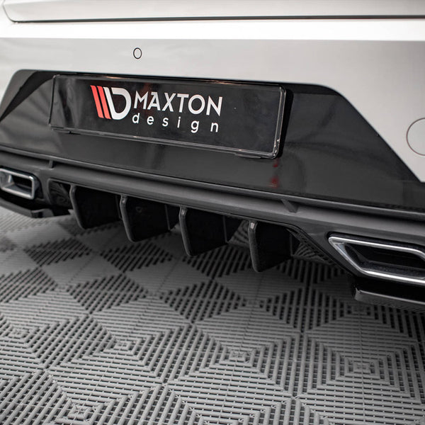 Car's rear bumper features dual exhaust outlets and diffuser; black "MAXTON design" license plate is displayed; parked on textured gray flooring in an indoor setting.