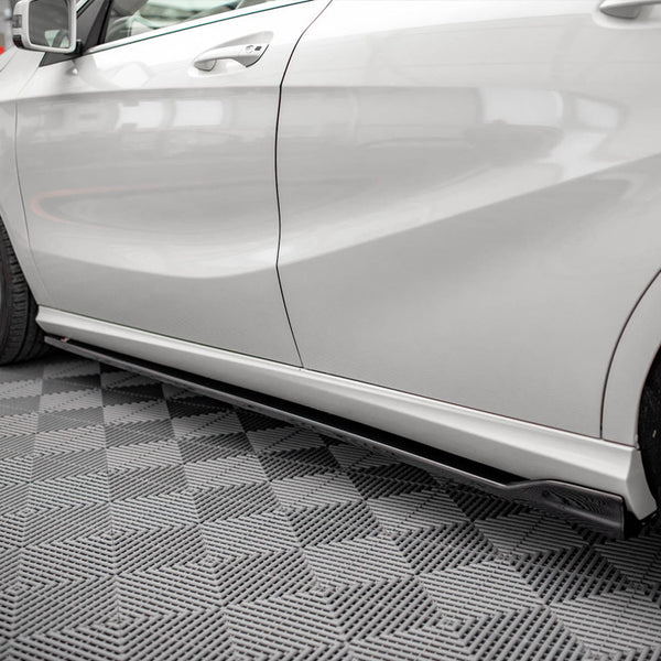 White car parked indoors, highlighting its sleek side profile with aerodynamic contours. The floor has a gray geometric patterned design, and the vehicle rests in a well-lit garage setting.