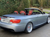 Convertible BMW with red interior parked on a driveway, surrounded by lush hedges and trees. The rear license plate reads 
