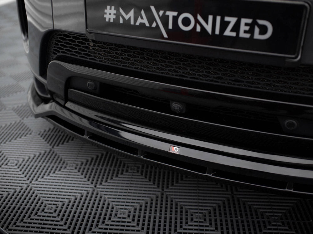 A black car's front bumper displays the text "#MAXTONIZED" on a license plate with a hexagonal grille, parked on a patterned rubber mat.